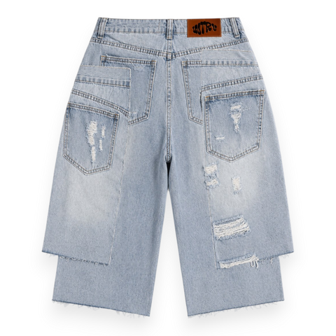 Back view of INTROVERT men's double waistband denim shorts showing the layered raw-edge paneling, asymmetric pocket details, and a brown leather INTRV logo patch.