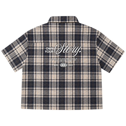 Back view of INTRV "Story" short sleeve charcoal-navy plaid flannel shirt highlighting the premium white screen-printed "Own Your Story" graphic layout.