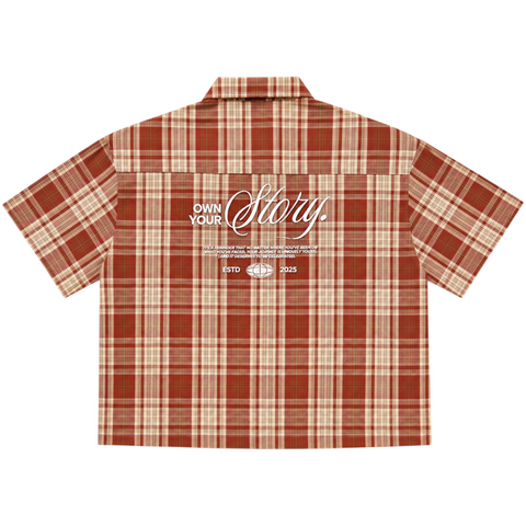 Back view of INTRV "Story" short sleeve red-brown plaid flannel shirt showcasing the white screen-printed "Own Your Story" graphic typography layout across the upper back.